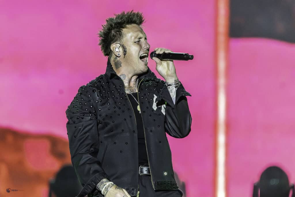 A man with tattoos singing into a microphone.